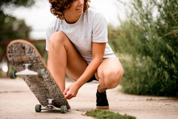 Νέα χαμογελαστή γυναίκα δένει τα κορδόνια στα παπούτσια της, ενώ skateboard στέκεται κοντά — Φωτογραφία Αρχείου