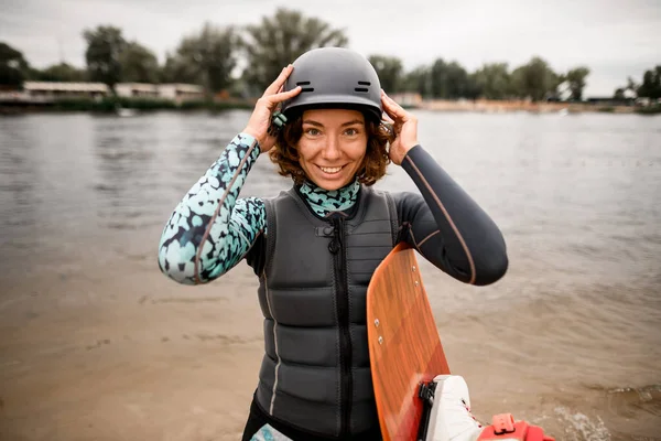 Vista frontale della giovane donna sorridente che indossa il giubbotto di salvataggio mettendo il casco sulla testa — Foto Stock