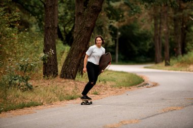 Aktif gülümseyen kadın elinde sörf tahtasıyla kaykaya biniyor.