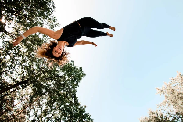 Lächelnde junge Frau springt und stolpert in die Luft gegen den blauen Himmel. — Stockfoto