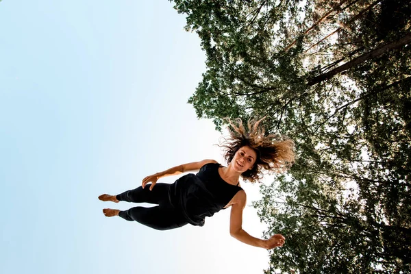 Glückliche junge Frau springt und taumelt in der Luft gegen den blauen Himmel. — Stockfoto