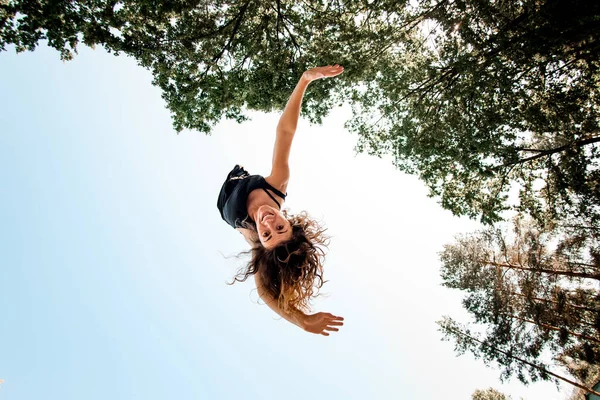 Bottom view of cheerful woman in the air against blue sky and green trees. — Stock Photo, Image