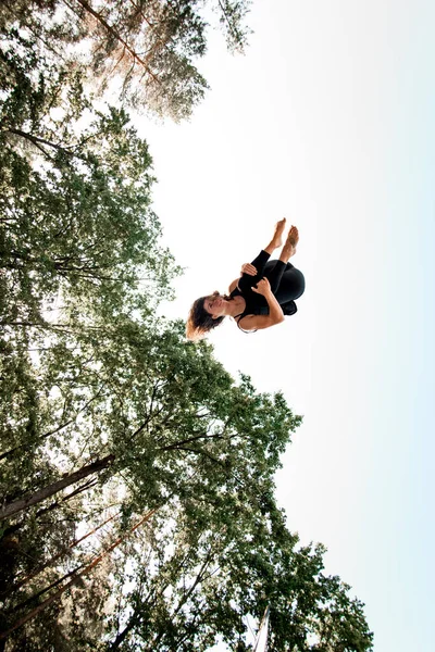 Mujer joven activa saltando alto y cayendo en el aire contra el cielo azul. —  Fotos de Stock
