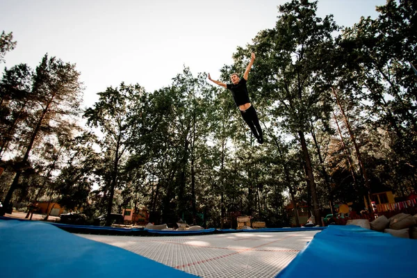 Sportler springt auf Trampolin vor der Kulisse grüner Bäume und des Himmels. — Stockfoto