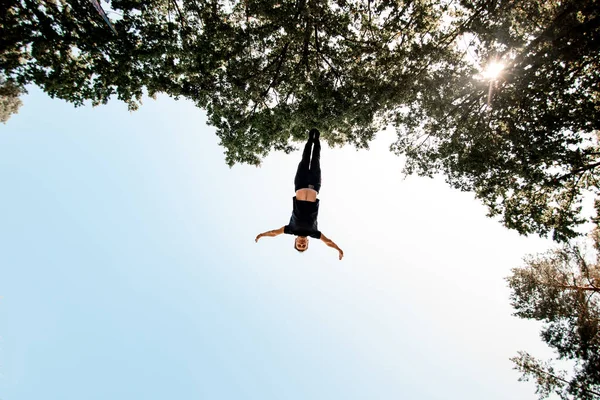 view of man jumps high in the air against blue sky and green trees.