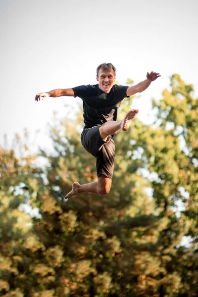 Fröhlicher junger Mann springt vor dem Hintergrund grüner Bäume in die Luft. — Stockfoto
