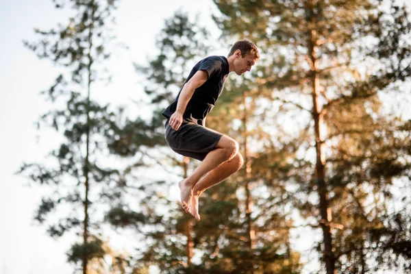 緑の木々を背景に空を飛び跳ねる男の側面図 — ストック写真