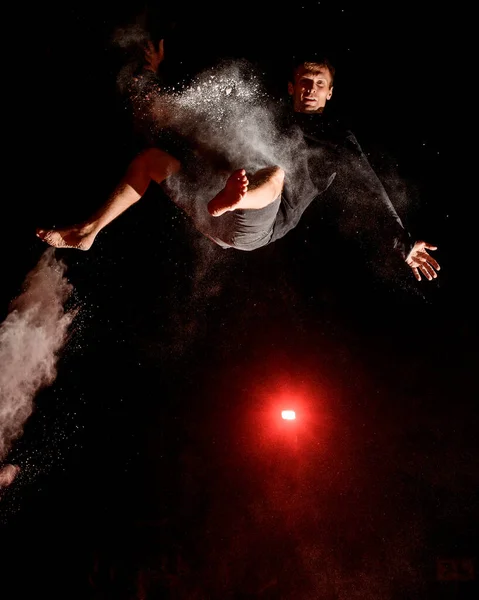 若い男が空高くジャンプし、サーチライトの光が彼を照らす — ストック写真