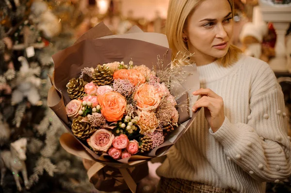 Mujer rubia sosteniendo ramo de rosas decoradas con bayas y conos dorados — Foto de Stock