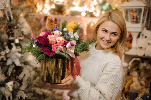 Χαμογελαστή ξανθιά γυναίκα κρατώντας κουτί με λουλούδι ρύθμιση με πευκοβελόνες και πουλιά παιχνίδι — Φωτογραφία Αρχείου