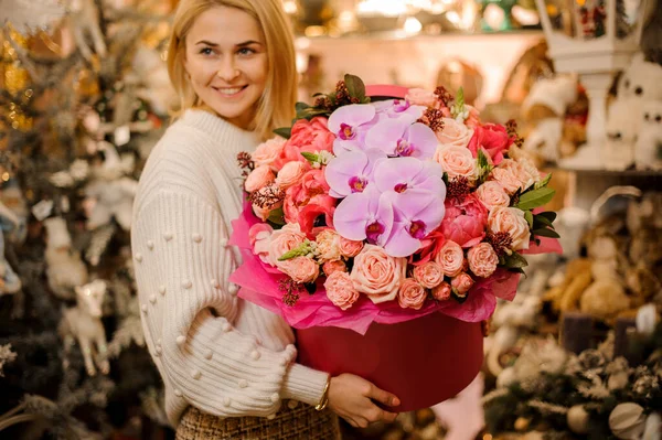 Усміхнена жінка тримає велику круглу червону коробку з букетом з орхідей і півоній і троянд — стокове фото