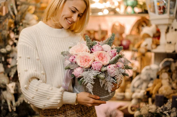 Νεαρή χαμογελαστή γυναίκα κρατώντας κουτί με λεπτή σύνθεση από ροζ λουλούδια και κλαδιά πεύκου — Φωτογραφία Αρχείου