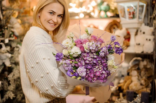 Mujer rubia sonriente sosteniendo hermoso ramo de flores de color púrpura variedad — Foto de Stock