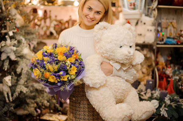 Ευτυχισμένη γυναίκα κρατώντας λευκό αρκουδάκι και μπουκέτο από φρέσκα φωτεινά ανοιξιάτικα λουλούδια — Φωτογραφία Αρχείου
