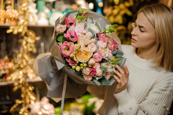 Floristería mujer joven sostiene ramo de flores blancas y rosadas y lo mira — Foto de Stock