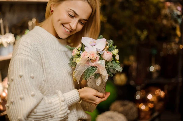 Mujer sonriente sostiene composición de flores y ramas de abeto decoradas con juguetes de Navidad — Foto de Stock