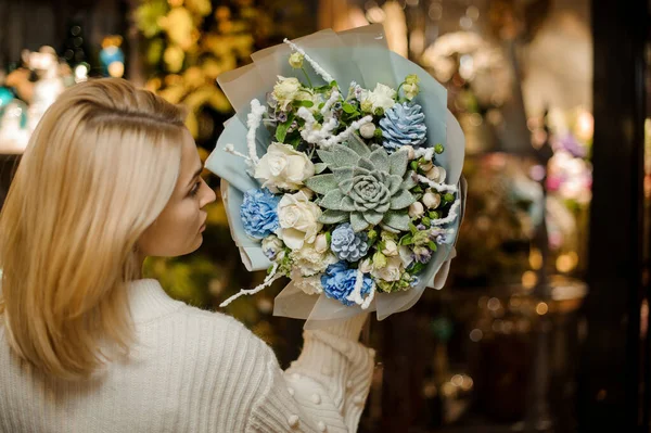 밝은 빛으로 장식 된 파란색 색조의 꽃과 식물들로 꽃다발을 이룬 금발 여자. — 스톡 사진