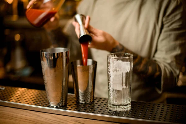 Бармен майстерно наливає червоний напій з металевого лобзика в шейкер на барній стійці — стокове фото