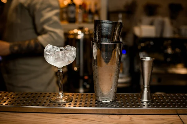 Bicchiere di vino con cubetti di ghiaccio e shaker e jigger sono sul bar. — Foto Stock