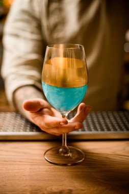 Barın üzerinde duran altın madalyayla süslenmiş mavi kadehli erkek eli.