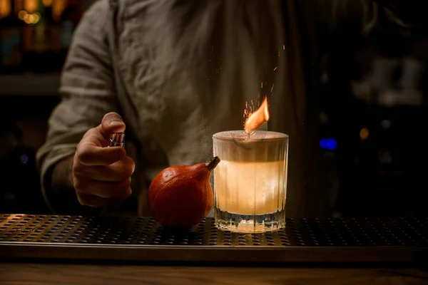 Man carefully sprinkles on old fashioned glass of cocktail with foam and with burning leaf. — Stock Photo, Image