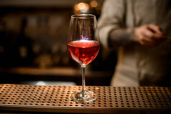 Gelas anggur dengan minuman transparan merah terang berdiri di meja bar. — Stok Foto