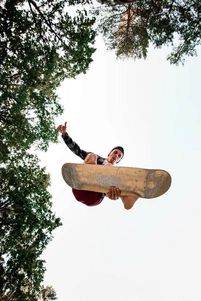 Vista inferior del hombre con simulador de skate saltando sobre el fondo del cielo azul —  Fotos de Stock