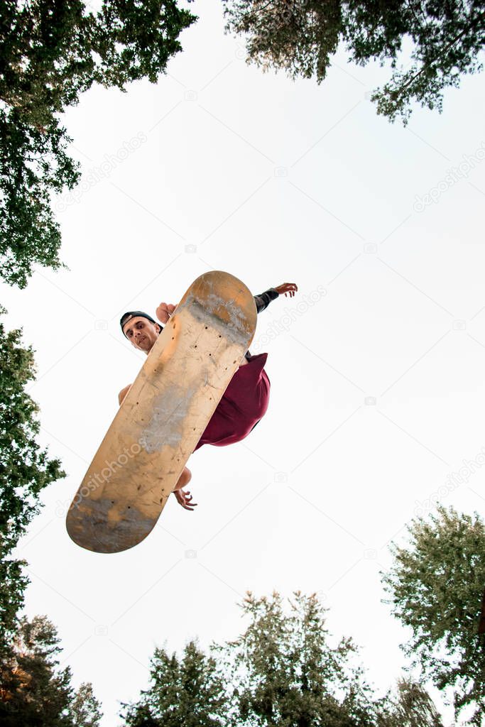 bottom view of sportsman with skate simulator jumping up against background of blue sky