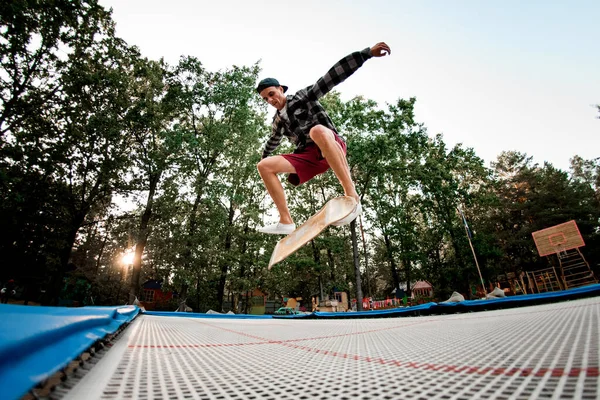 Смотреть молодой парень активно прыгает со скейтборда на батуте — стоковое фото