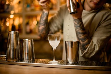 Barmen barın tezgahındaki bardağa metal jigger 'dan su dolduruyor.