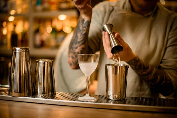 Vy på bardisken bakom vilken bartendern häller vätska från jigger i mätbägare. — Stockfoto