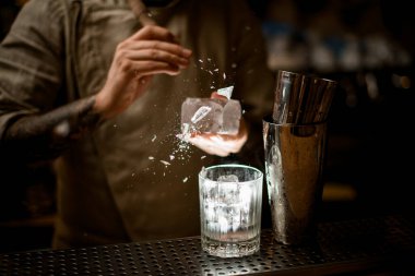 İnsan buzu tutar ve ustalıkla parçalara ayırır ve bardaklar yakınlarda durur.