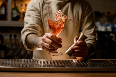 Barmen elinde zencefil ve kokteyl bardağı tutuyor. Elinde de alkollü içki var.