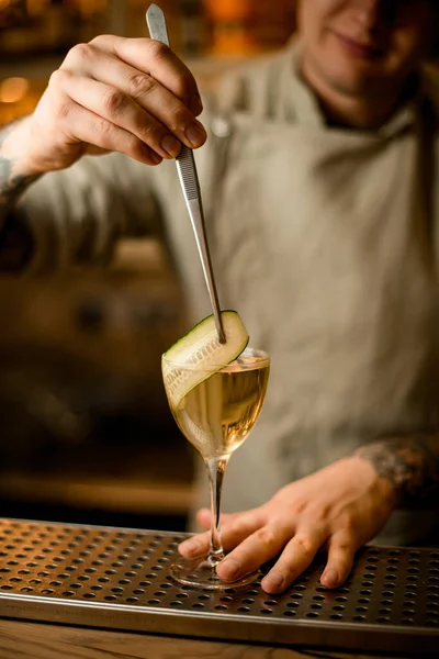 Barman decora copa de cóctel con rodaja de pepino con pinzas — Foto de Stock