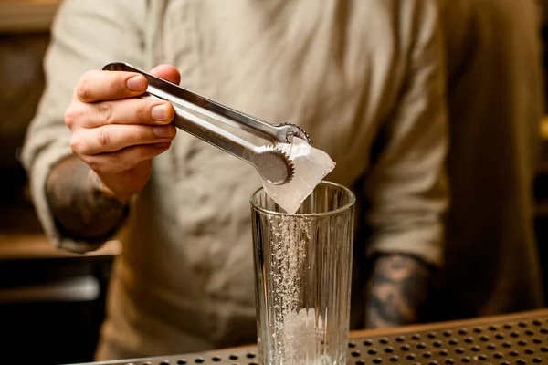 Чоловік бармен тримає щипці в руці з кубиком льоду над склом на барі — стокове фото