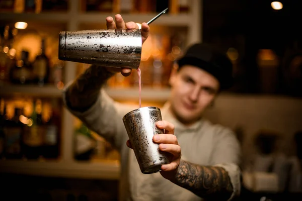 Joven barman sostiene vasos de coctelera en sus manos y vierte beber de ellos — Foto de Stock