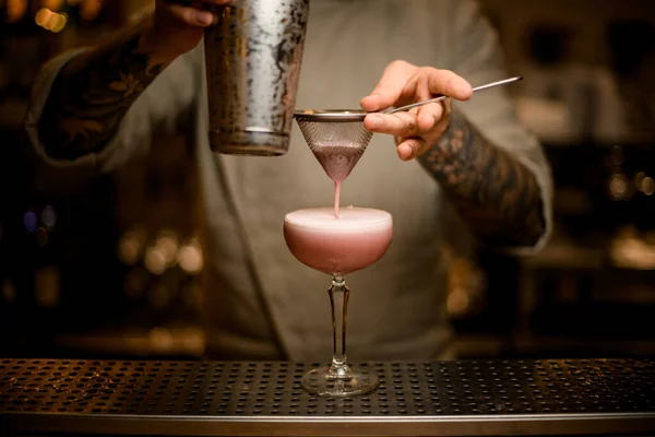 Man bartender filter vispad cocktail genom såll i vinglas på bar disk — Stockfoto