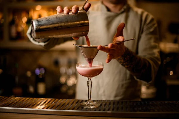 Camarero masculino sostiene tamizar sobre la copa de vino y vierte suavemente cóctel de coctelera. — Foto de Stock