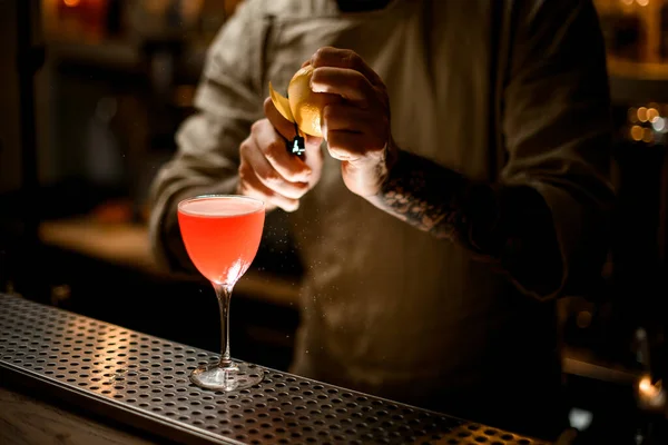 Vista en barman sostiene limón y precisa corta la cáscara con cuchillo — Foto de Stock