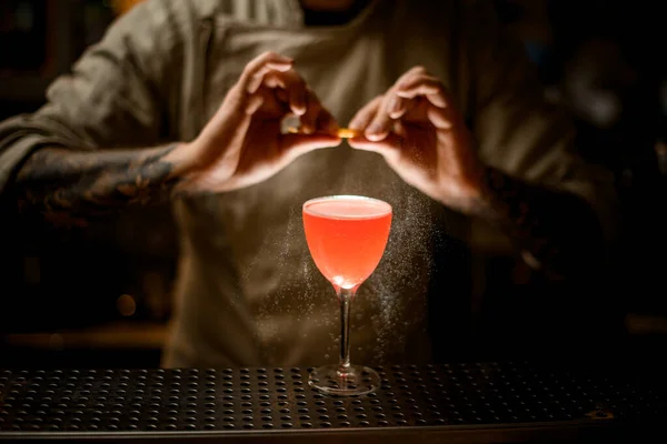 Barman drží citrónovou kůru a obratně sype na sklo s jasným koktejlem. — Stock fotografie