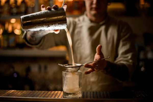 Barkeeper hält Sieb über altmodisches Glas und gießt Cocktail aus Shaker. — Stockfoto