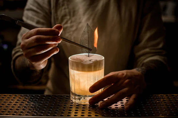 Camarero hombre sostiene pinzas con hoja ardiente para decorar vaso de cóctel — Foto de Stock