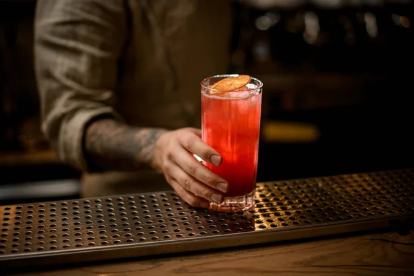 Mans hand houdt glas met koude drank met ijsblokjes, versieren met sinaasappelschijfje — Stockfoto