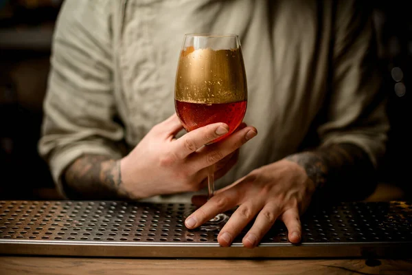 Manos masculinas sosteniendo copa de vino con bebida gaseosa decorada con oro de pie en la barra — Foto de Stock