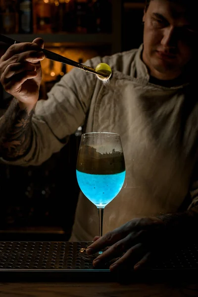 Bartender accurate holds golden piece of ice over steaming wine glass and look at it — Stock Photo, Image