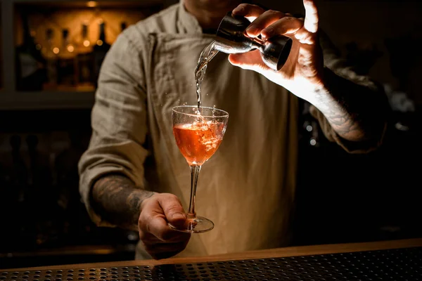 Mannelijke barman houdt met de hand wijnglas met drank en voegt vloeistof van jigger — Stockfoto