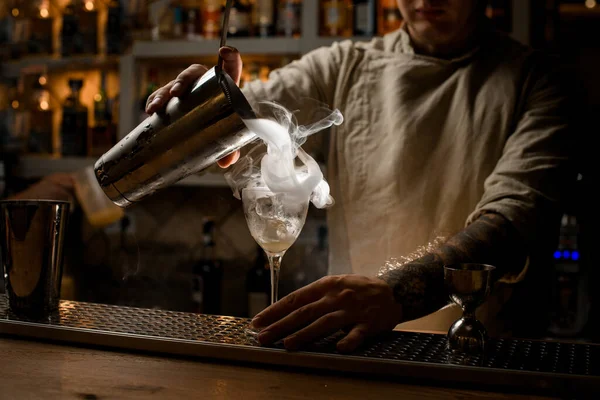 Vista del camarero macho vertiendo bebida humeante de la taza de coctelera en copa de vino — Foto de Stock