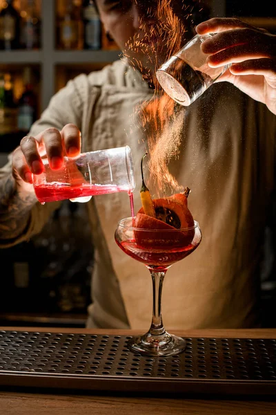 Barman voegt meesterlijk ingrediënten toe aan glas met groenten erin en maakt er vuur over — Stockfoto