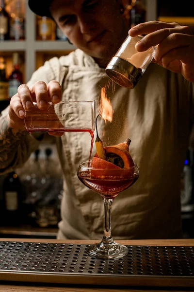 Barman nauwkeurige ingrediënten toe te voegen aan glas met groenten binnen en maakt vuur over het — Stockfoto