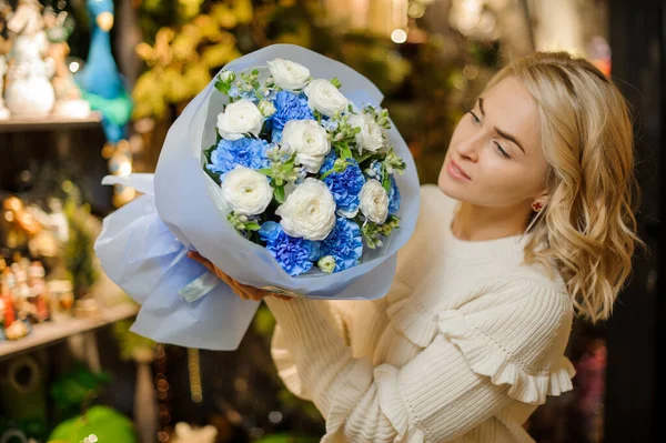 Mujer rubia sostiene ramo de flores de rosas blancas y claveles azules brillantes — Foto de Stock